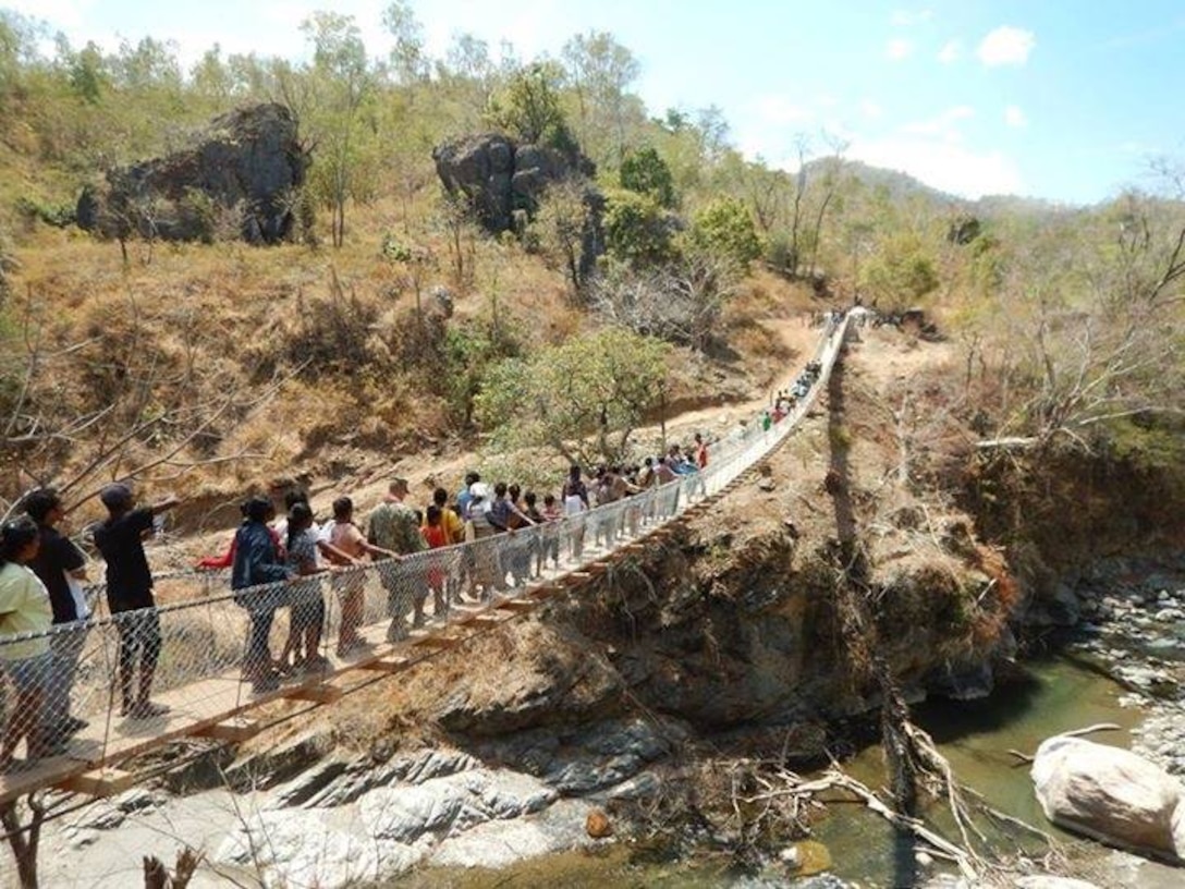 Pedestrians cross the completed bridge constructed by the Naval Mobile Construction Battalion 5's Construction Civic Action Detail in the Democratic Republic of Timor-Leste.