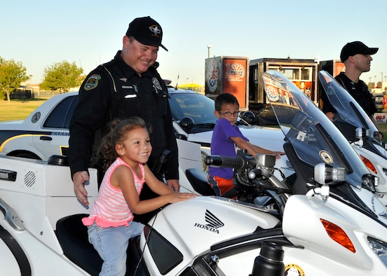 A police officer watches as a child smiles for a photo on his police motorcycle during the Deployed Family Day September 25, 2015, at Fowler Park on Luke Air Force Base, Arizona. Families enjoyed an evening of bounce houses, K-9 play time, food, music and togetherness during their spouse’s separation. (U.S. Air Force photo by Staff Sgt. Marcy Copeland)