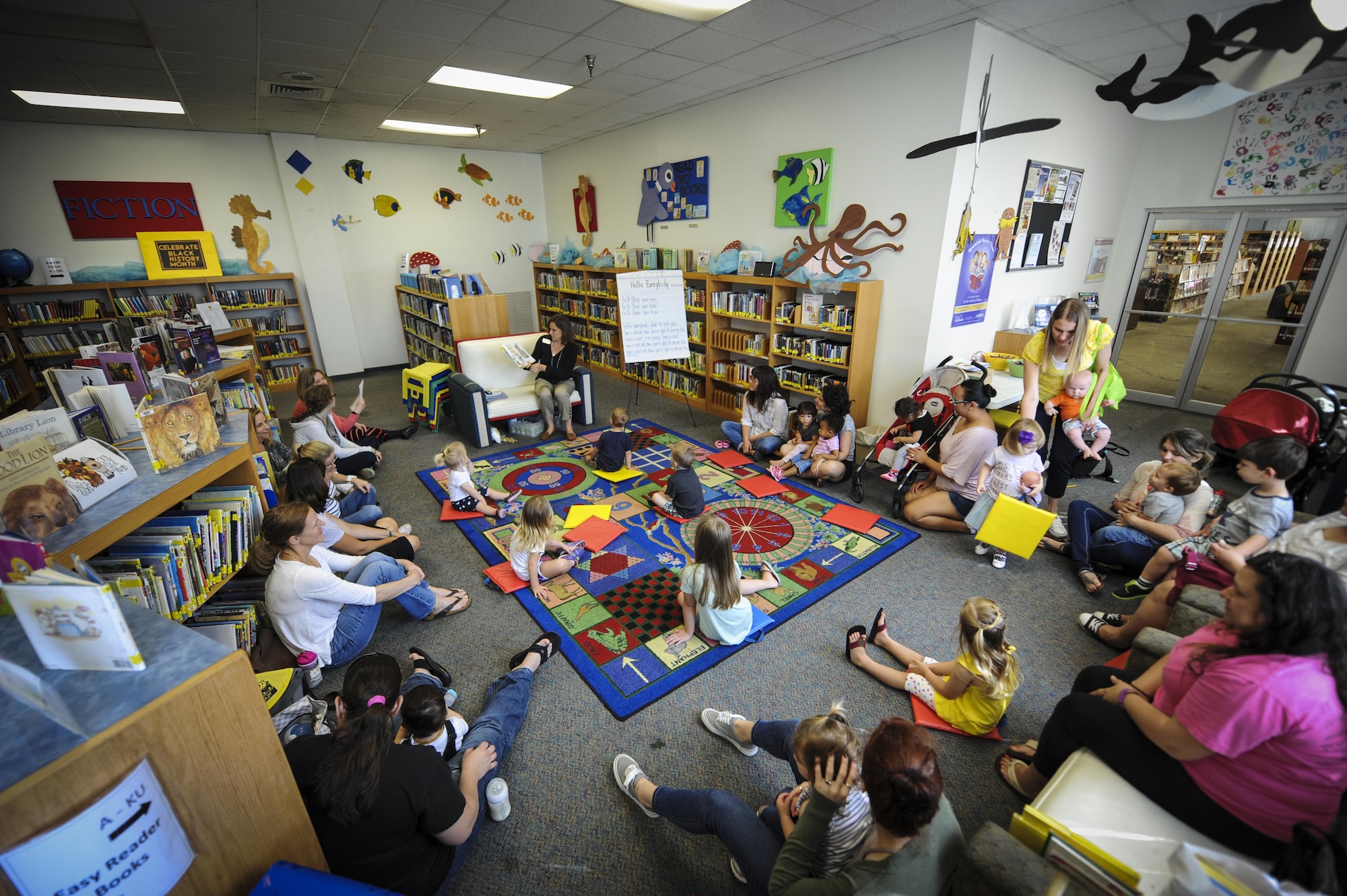 Visiting parents and children listen to a story during reading time at the library, Hurlburt Field, Fla., March 31, 2016. Every Thursday, there is a reading time that hosts a guest speaker to read to children. During the event, there are songs and physical activities, as well as a craft time after the stories for children and parents to participate in. The goal is to help children work on literacy skills, fine motor capabilities and social skills. (U.S. Air Force photo by Senior Airman Meagan Schutter)