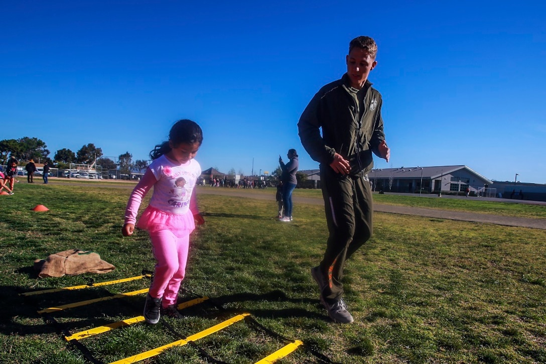 MARINE CORPS BASE CAMP PENDLETON, Calif. – Lance Cpl. George Cofield, right, guides Samantha Torres through an obstacle course at North Terrace Elementary, March 25, 2016. Approximately 30 Marine volunteers with the Single Marine Program facilitated a series of exercises and competitions including an obstacle course relay race and tug-of-war as part of a Physical Education Fitness Challenge. The challenge encourages children to stay active and helps Marines engage with their local community. Cofield, a native of Windsor, Va., is an aviation mechanic with Marine Aviation Logistics Squadron 39, Marine Aircraft Group 39, 3rd Marine Aircraft Wing, I Marine Expeditionary Force. Torres is a kindergarten student at North Terrace Elementary. (U.S. Marine Corps photo by Lance Cpl. Caitlin Bevel/RELEASED)