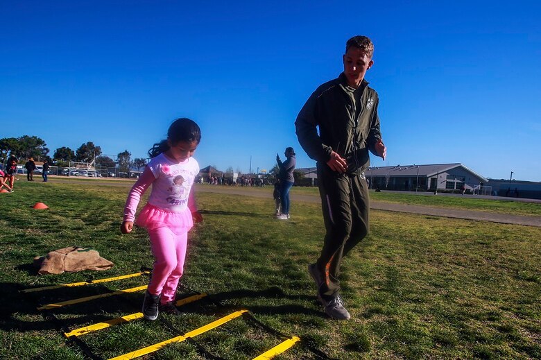 MARINE CORPS BASE CAMP PENDLETON, Calif. – Lance Cpl. George Cofield, right, guides Samantha Torres through an obstacle course at North Terrace Elementary, March 25, 2016. Approximately 30 Marine volunteers with the Single Marine Program facilitated a series of exercises and competitions including an obstacle course relay race and tug-of-war as part of a Physical Education Fitness Challenge. The challenge encourages children to stay active and helps Marines engage with their local community. Cofield, a native of Windsor, Va., is an aviation mechanic with Marine Aviation Logistics Squadron 39, Marine Aircraft Group 39, 3rd Marine Aircraft Wing, I Marine Expeditionary Force. Torres is a kindergarten student at North Terrace Elementary. (U.S. Marine Corps photo by Lance Cpl. Caitlin Bevel/RELEASED)
