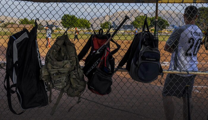 Duffle bags hang on the fence as a member of the 57th Operations Support Squadron intramural softball team waits for his turn to bat during a practice game at Nellis Air Force Base, Nev., March 29, 2016. Softball games, which are held Monday through Thursday from 5:30 to 7:30 p.m., are meant to build goodwill between the units. (U.S. Air Force photo by Airman 1st Class Kevin Tanenbaum)