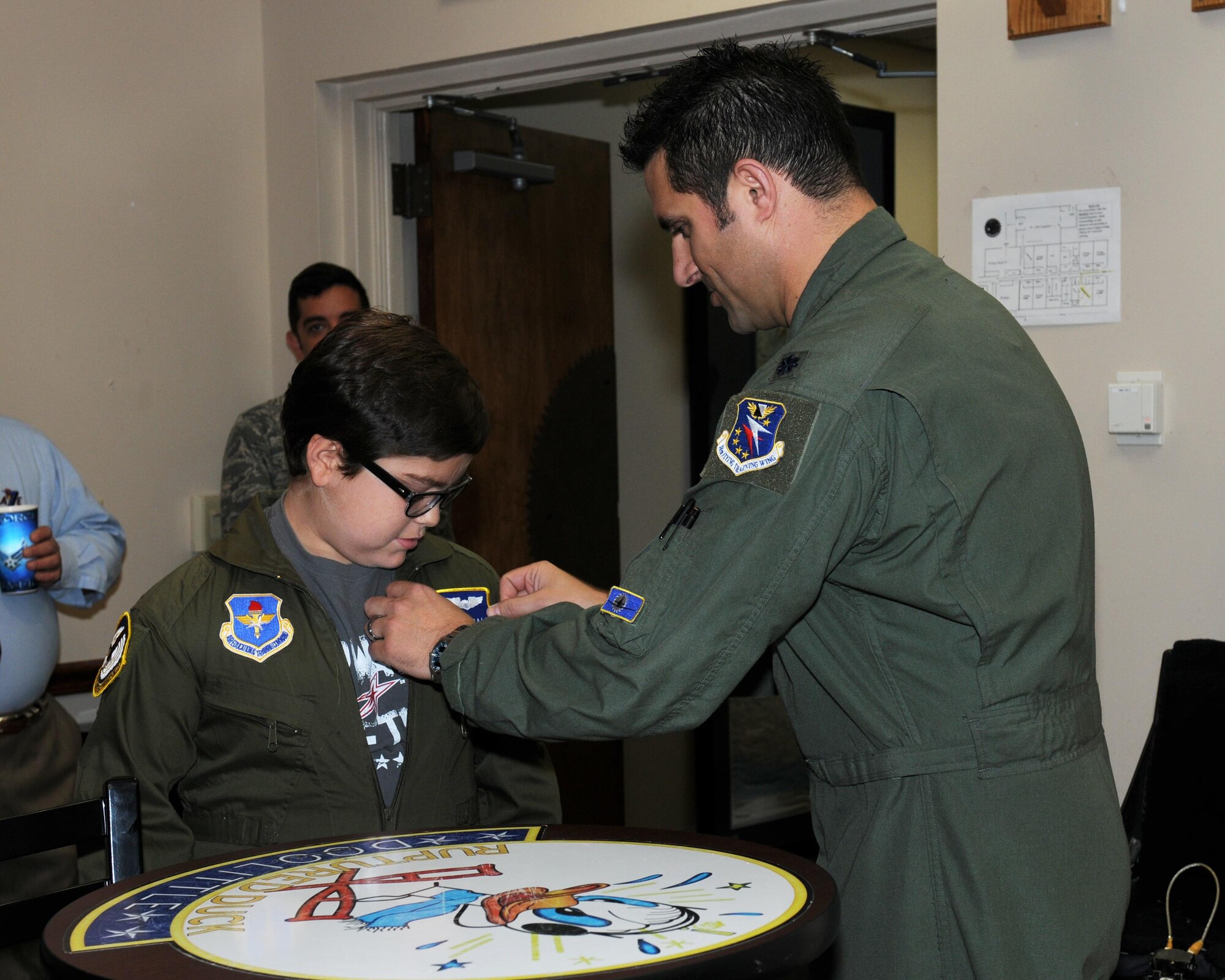 Lt. Col. Kirby Ensser, 41st Flying Training Squadron Commander, places a name tape on Andrew McCall, Pilot for a Day program participant, before his exciting day in the life of a pilot March 28 at Columbus Air Force Base, Mississippi. McCall and his family learned about the base’s mission, visited static aircraft displays, toured various units and ended the day “flying” in a T-6 Texan II simulator. (U.S. Air Force photo/Melissa Doublin)