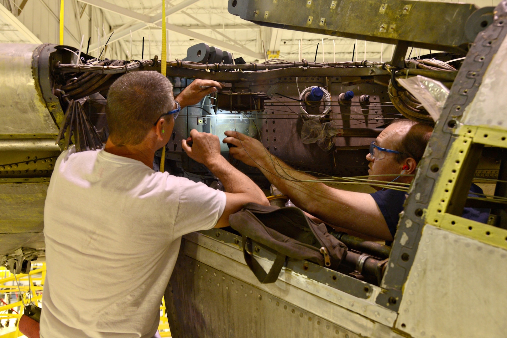 Chris Carson and Martin Harpster, both aircraft mechanics with the 565th Aircraft Maintenance Squadron, work on throttle cable pullies on the right wing of “Ghost Rider.” (Air Force photo by Kelly White/Released)
