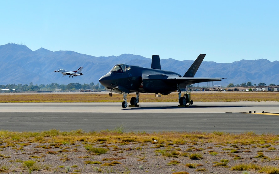 An F-35A Lightning II Joint Strike Fighter parked on the flight line Apr. 2, 2016, while the U.S. Air Force Thunderbirds Demonstration Team perform overhead at 75 Years of Airpower (U.S. Air Force photo by Senior Airman James Hensley)