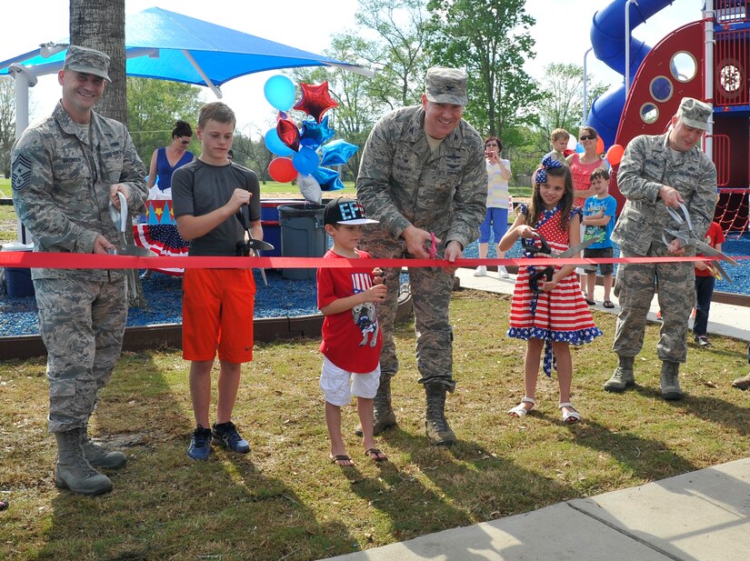 Children from Joint Base Charleston families help Chief Master Sgt. Mark Bronson, 628th Air Base Wing command chief (left), Col. Robert Lyman, Joint Base Charleston commander (center) and Col. Richard Mathews, 628th Mission Support Group commander (right) cut the ribbon to open the new playground on Touhey Boulevard March 28, 2016. The playground includes two play areas, two tetherball poles, a basketball court and a zip line. (U.S. Air Force photo/Airman Megan Munoz)