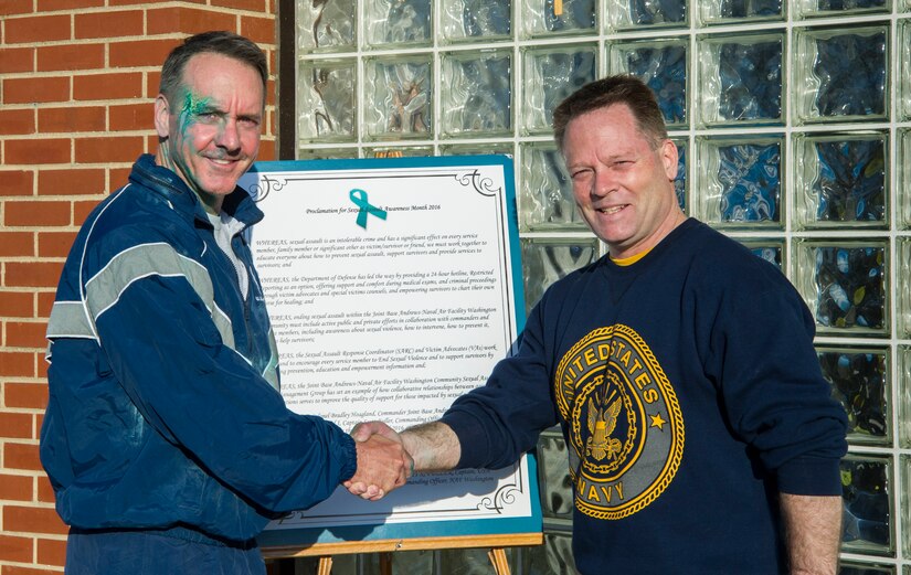 Col. Brad Hoagland (left), 11th Wing/Joint Base Andrews commander, and Capt. Scott Fuller, Naval Air Facility Washington commanding officer, shake hands and pose after signing a proclamation here, April 4, 2016. The event signified the recognition of April as Sexual Assault Awareness Month. (U.S. Air Force photo by Senior Airman Ryan J. Sonnier/RELEASED)