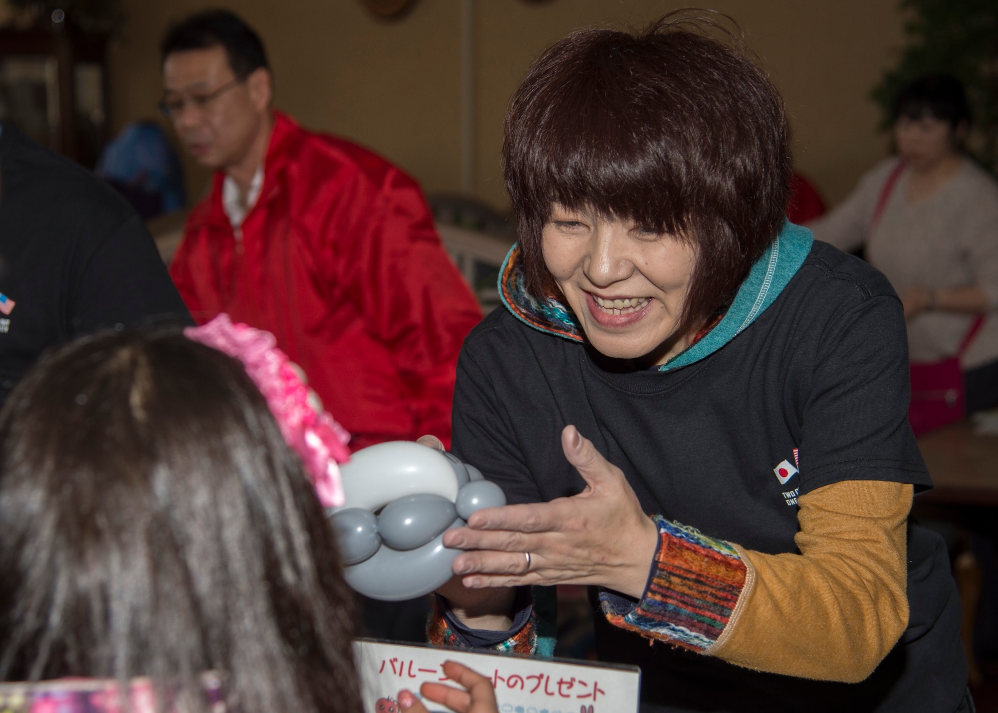 A 29th Annual Japan Day volunteer presents a balloon animal monkey to a child at Misawa Air Base, Japan, April 2, 2016. Multiple booths were on display highlighting Japanese culture for Misawa’s service members and families. (U.S. Air Force photo by Airman 1st Class Jordyn Fetter)