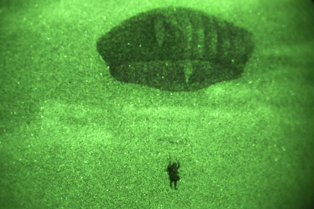 As seen through a night-vision device, a paratrooper descends through the sky during a night airborne operation onto Malemute drop zone at Joint Base Elmendorf-Richardson, Alaska, March 31, 2016. Air Force photo by Alejandro Pena