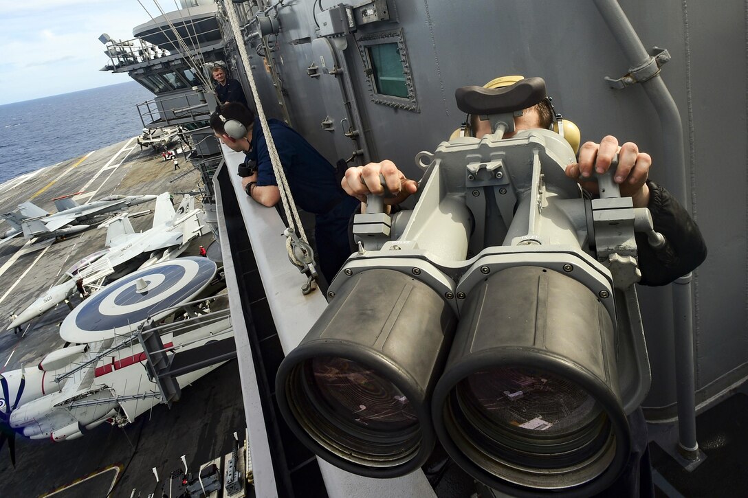 Seaman Fabian Soltero looks through shipboard binoculars aboard the aircraft carrier USS Dwight D. Eisenhower in the Atlantic Ocean, March 25, 2016. Soltero is a logistics specialist. Navy photo by Petty Officer 3rd Class Taylor L. Jackson
