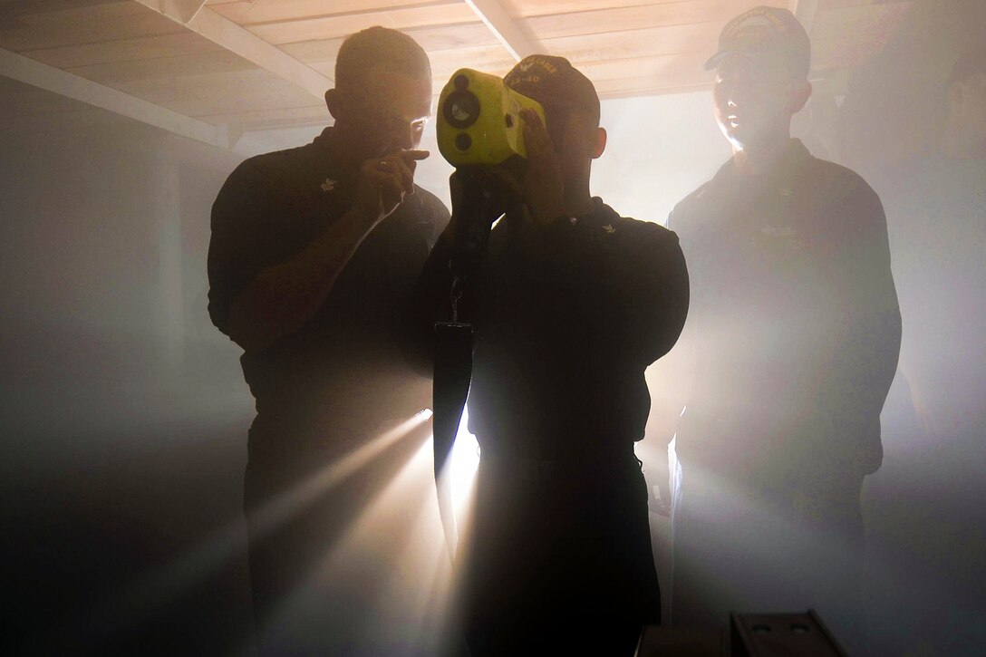 Navy Petty Officer 1st Class Michael Richmond, left, teaches Petty Officer 3rd Class John Paul Delossantos, center, how to operate a thermal imager while engulfed in mock smoke during a fast cruise in Polaris Point, Guam, Apr. 5, 2016. The fast cruise trains sailors in damage control, personnel accountability and various emergency situations. Navy photo by Petty Officer 2nd Class Jonathan T. Erickson