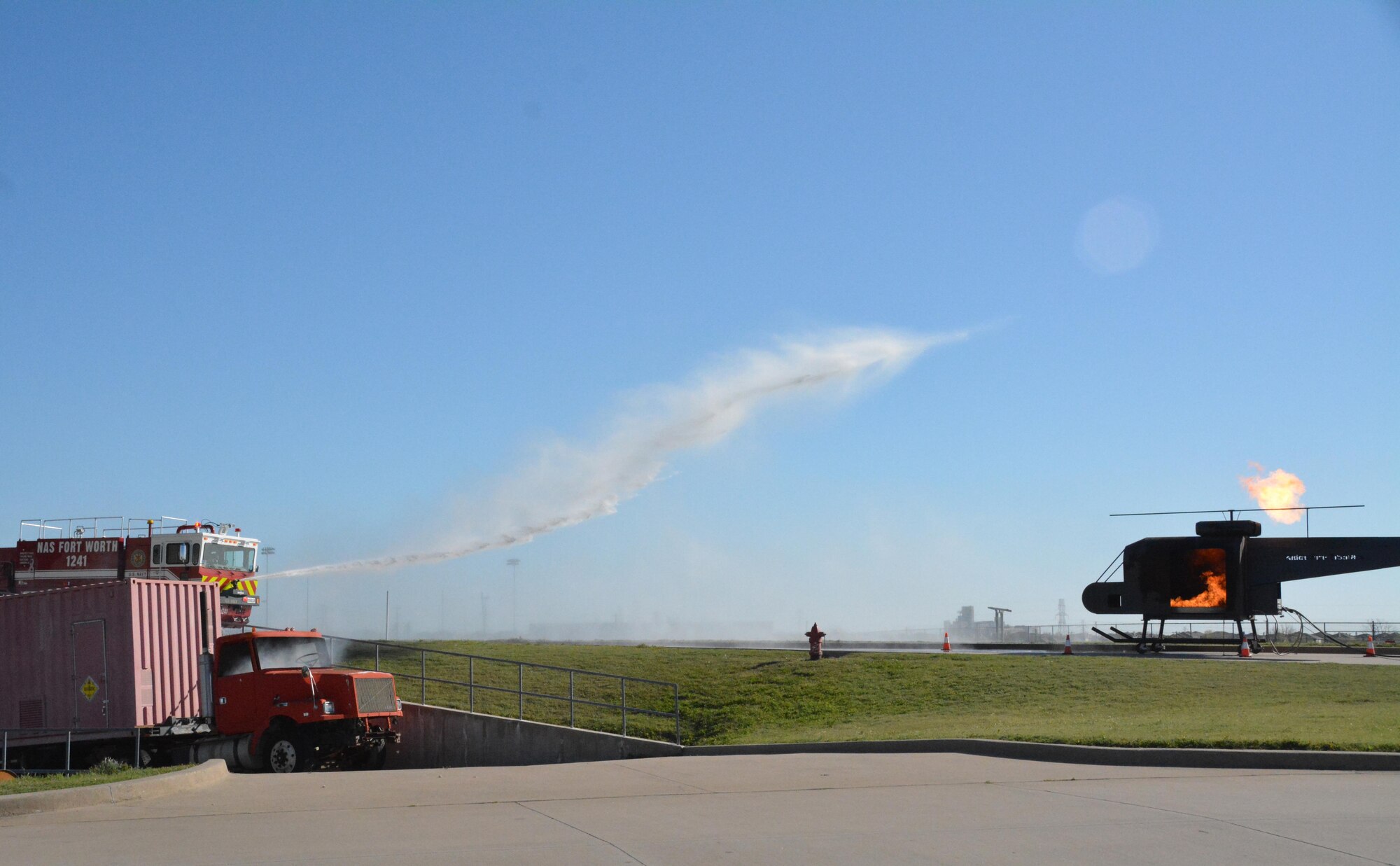 Naval Air Station Fort Worth Joint Reserve Base Fire Department sprays water March 22 towards an aircraft fire training simulator at Tarrant County College, Fort Worth, Texas, as part of an exercise scenario involving a crashed F-16. More than 150 firefighters, police, paramedics and military members participated in order to hone interagency collaboration and teamwork. (U.S. Air Force photo by Staff Sgt. Samantha Mathison)