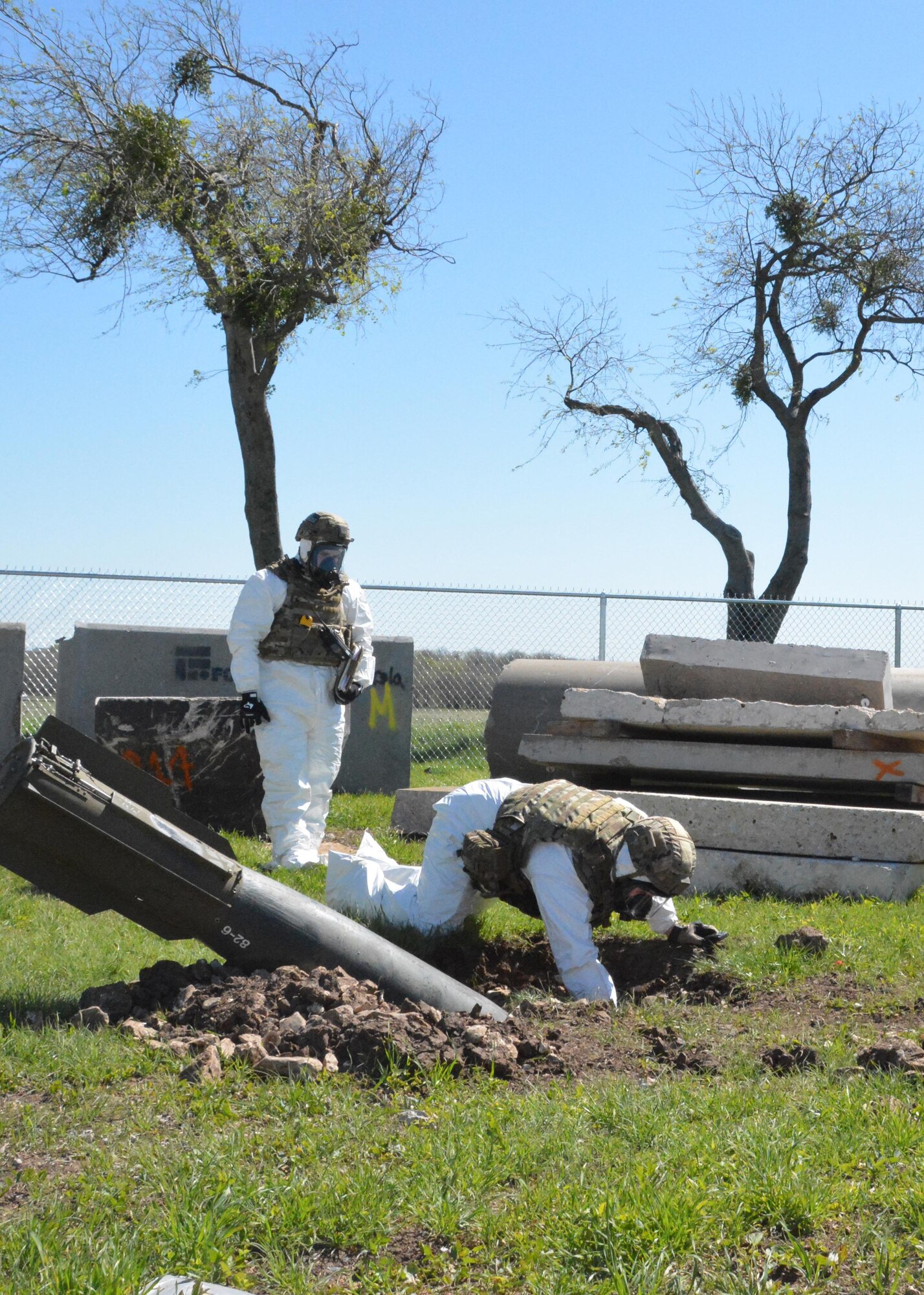 Staff Sgt. Chris Dolan, 301st Explosive Ordnance Disposal Flight technician, reaches into a crater where a training bomb lays at Tarrant County College, Fort Worth, Texas, while Senior Airman Jacob Atteberry, 301st EOD Flight technician, watches, March 22. The training bomb was one of two placed on the college’s northwest campus for the EOD team to practice disarming procedures. (U.S. Air Force photo by Staff Sgt. Samantha Mathison)