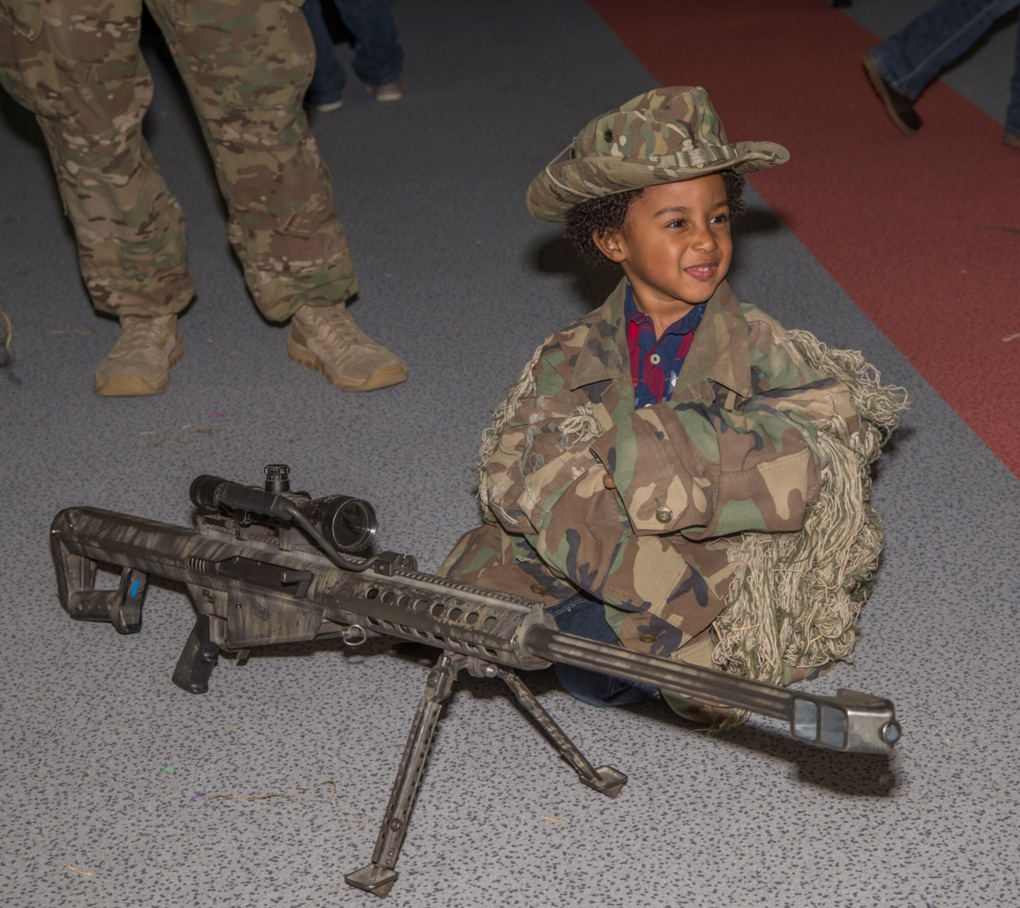 A Minot Youth Center member sits with a Missile Security Forces Squadron member’s rifle during the Eggstravaganza at Minot Air Force Base, N.D., March 25, 2016. The 91st MSFS tactical response force held a display at the event to educate and entertain participating youth. (U.S. Air Force photo/Airman 1st Class Christian Sullivan)