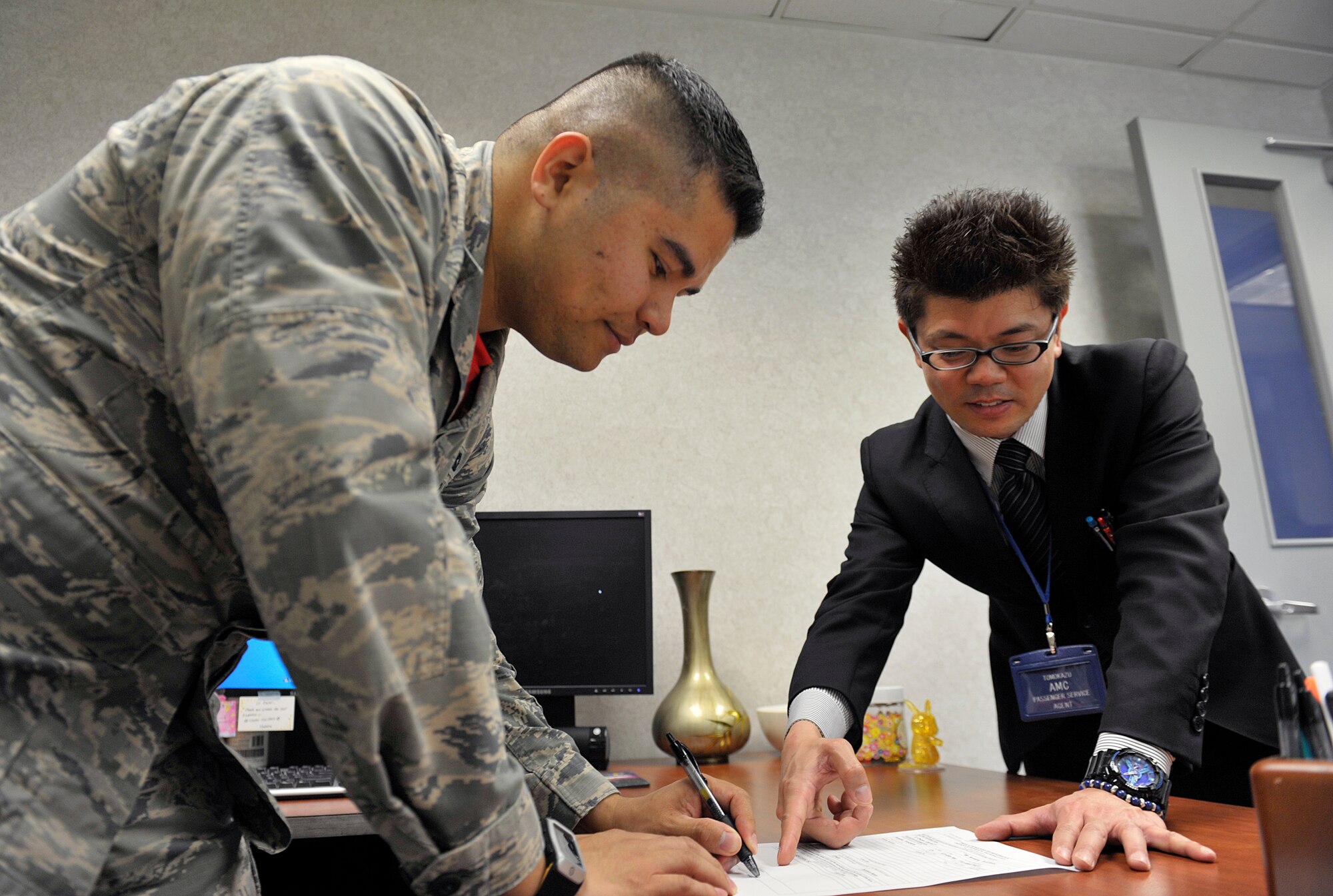 U.S. Air Force 1st Lt. Daniel Dwyer, 733rd Air Mobility Squadron passenger service office in charge, signs an unfunded environmental and morale leave form for Tomokazu Arakaki, 733rd AMS passenger service agent, April 1, 2016, at Kadena Air Base, Japan. Arakaki enjoys his job because he has been interested in working at the Airport since he was a student. (U.S. Air Force photo by Naoto Anazawa)
