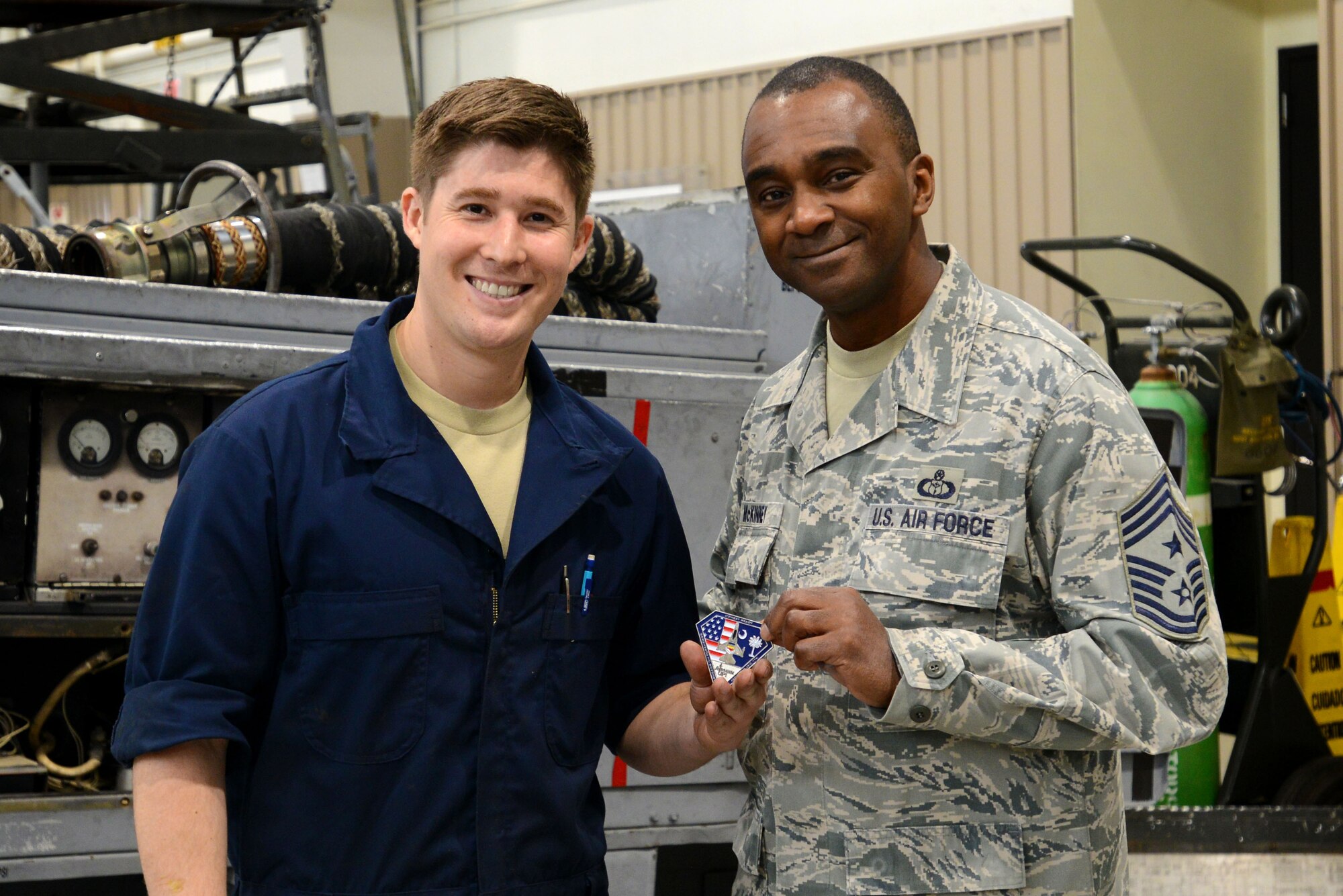 U.S. Air Force Airman 1st Class Kristofer Kabalan, 20th Equipment Maintenance Squadron aerospace ground equipment apprentice, receives a coin from Chief Master Sgt. Christopher McKinney, 20th Fighter Wing command chief, at Shaw Air Force Base, S.C., March 29, 2016. Kabalan spent the morning with McKinney, showing him how to service some AGE equipment by replacing oil filters and cleaning tire bearings. (U.S. Air Force photo by Airman 1st Class Kelsey Tucker)