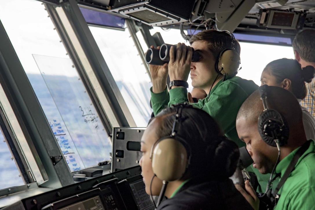 Navy Petty Officer 2nd Class Steven Martin uses binoculars to inspect the flight deck arresting gear wires from primary flight control aboard the aircraft carrier USS Dwight D. Eisenhower in the Atlantic Ocean, March 30, 2016. Martin is an aviation boatswain's mate equipment. Navy photo by Petty Officer 3rd Class Anderson W. Branch