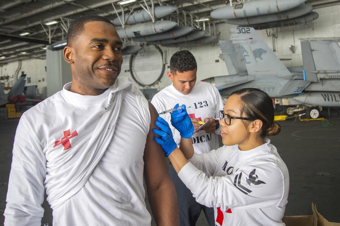 Navy Petty Officer 2nd Class Eunice Arnold, right, gives a shot to Petty Officer 1st Class Dishern Tucker in the hangar bay of the aircraft carrier USS Dwight D. Eisenhower in the Atlantic Ocean, April 4, 2015. The Dwight D. Eisenhower is preparing for a deployment. Navy photo by Seaman Matthew Thompson