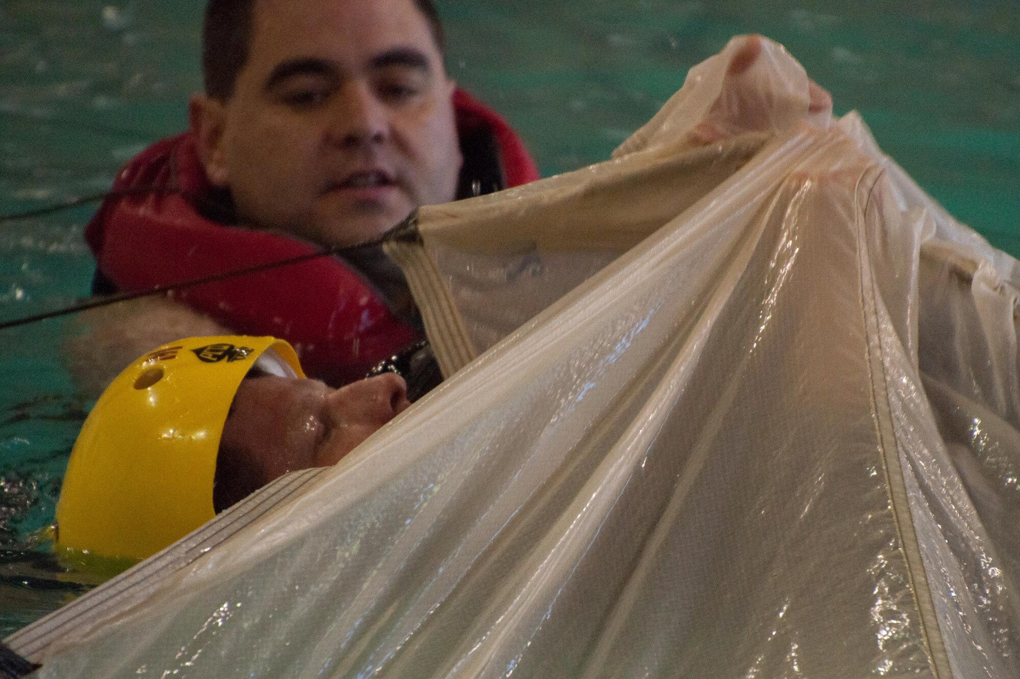 A U.S. Air Force aircrew member of the 307th Bomb Wing pulls himself out from under a deployed parachute with the help of an Airman from the 307th Operational Support Squadron in a pool at the Louisiana State University, Shreveport, La. on April 3rd. All B-52 Stratofortress crewmembers are required to receive water survival training to practice what to do in the event of a waterborne landing. (U.S. Air Force photo by Master Sgt. Dachelle Melville/Released)