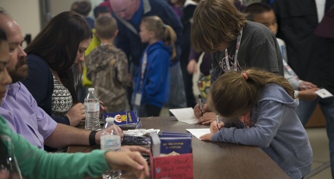 A child writes her name on her Gunfighter Jr. passport April 4, 2016, at Mountain Home Air Force Base, Idaho. Children of deployed service members had the opportunity to walk through a mock deployment line and experience the process of a deployment. (U.S. Air Force photo by Senior Airman Malissa Lott/RELEASED)