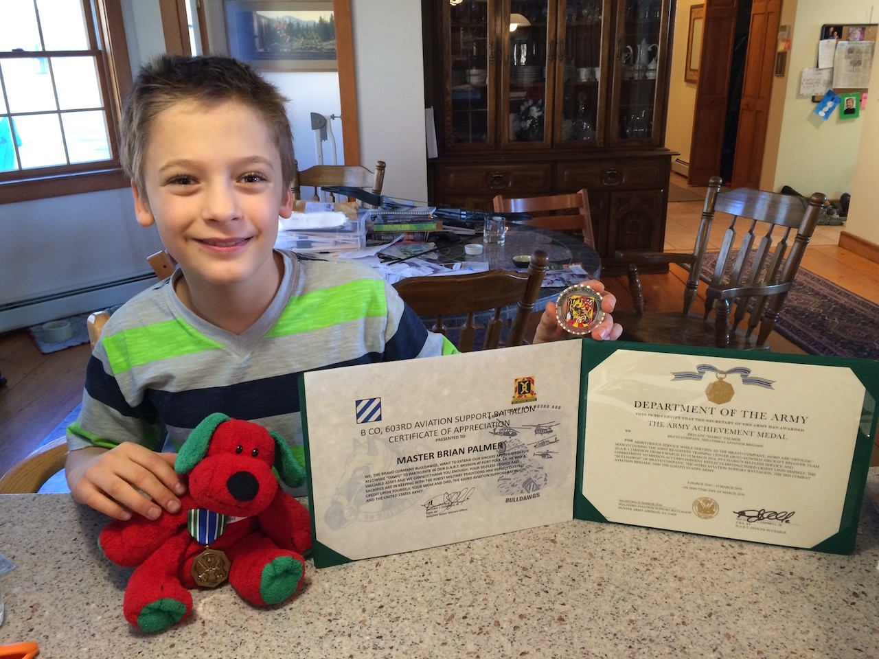 Bryan Palmer of Hanover, New Hampshire, holds his stuffed animal, Dawg, and the awards they received after they were reunited, March 26, 2016. Army Chief Warrant Officer 4 Michael Campbell, battalion senior warrant officer, 603rd Aviation Support Battalion, 3rd Combat Aviation Brigade, found Dawg at a hotel. The stuffed animal became a mascot for the unit until he could be returned to his owner. Courtesy photo by Elaine Palmer