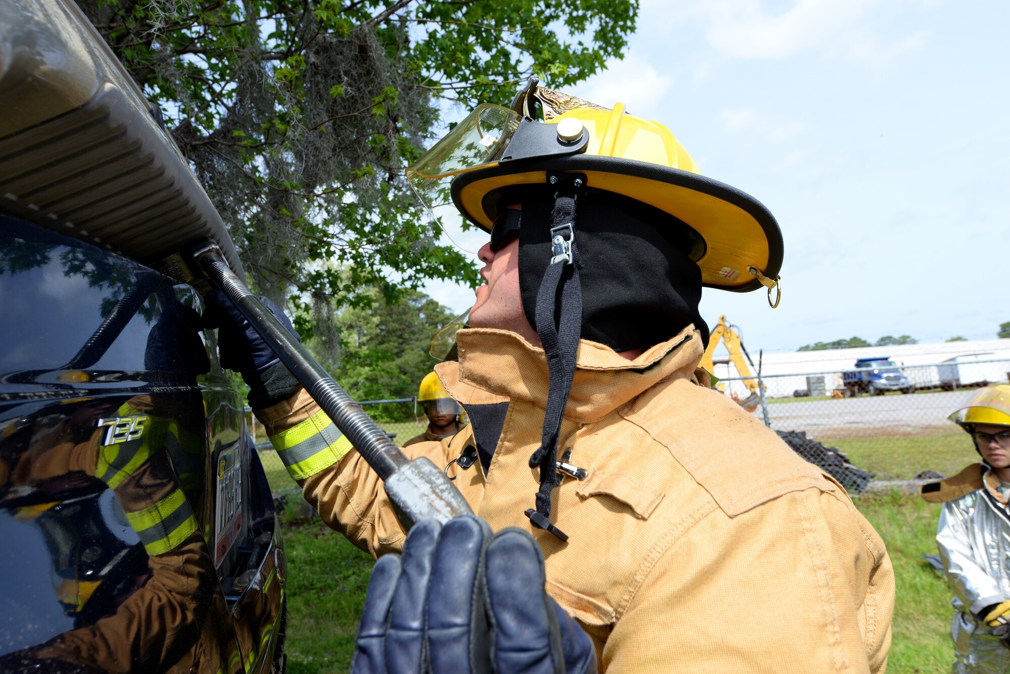 A picture of an airman utilizing a halligan tool to soften a vehicle.