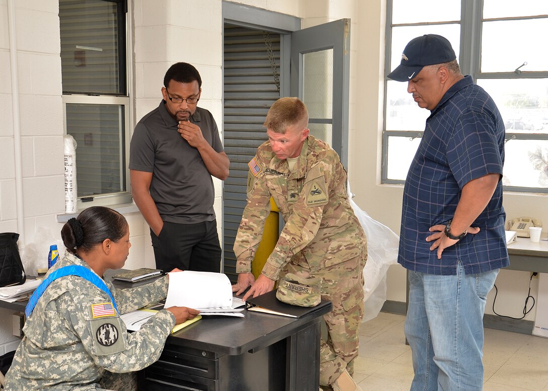 A soldier from the Army control cell (seated) disscuses paper work issues with another soldier while Jason Middleton, chief of the DLA Distribution expeditionary team (second from left) and DLA Disposition Services West Director Christopher “Buck” Buchanan (far right) listen in for the outcome. 