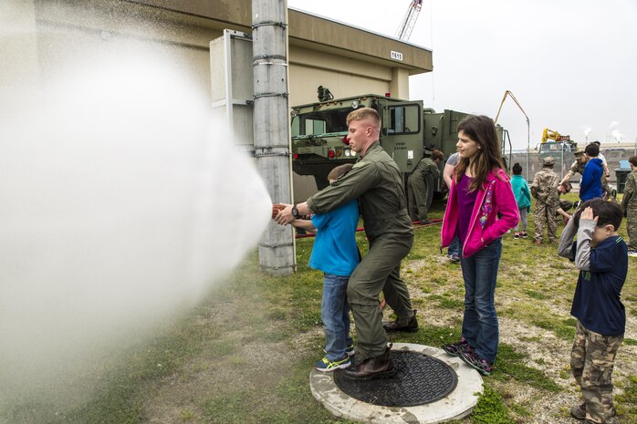 Sgt. Isaac Ross, aircraft rescue firefighter with Headquarters and Headquarters Squadron, helps a child with the fire hose during Junior Recruit Day at Marine Corps Air Station Iwakuni, Japan, April 8, 2016. Junior Recruit Day allowed the children of service member’s assigned Marine Aircraft Group 12 to get a first-hand look at what their military parent’s experiences on a daily basis. (U.S. Marine Corps photo by Sgt. Antonio J. Rubio)