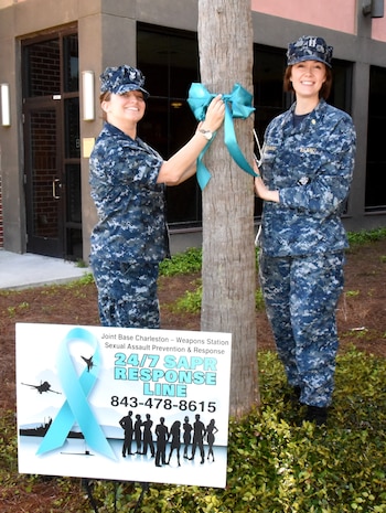 Hospital Corpsman 2nd Class Nicole Johnson, left, assistant command career counselor and victim advocate for Naval Health Clinic Charleston, and Lt. Nikki Pritchard, NHCC's Medical Homeport Blue Team leader and Sexual Assault Prevention and Response program coordinator, tie a teal ribbon on a tree in front of Naval Health Clinic Charleston April 4 in recognition of Sexual Assault Awareness Month. Throughout April, NHCC staff members commit to doing their part in preventing sexual assault. (Navy photo/ Kris Patterson)