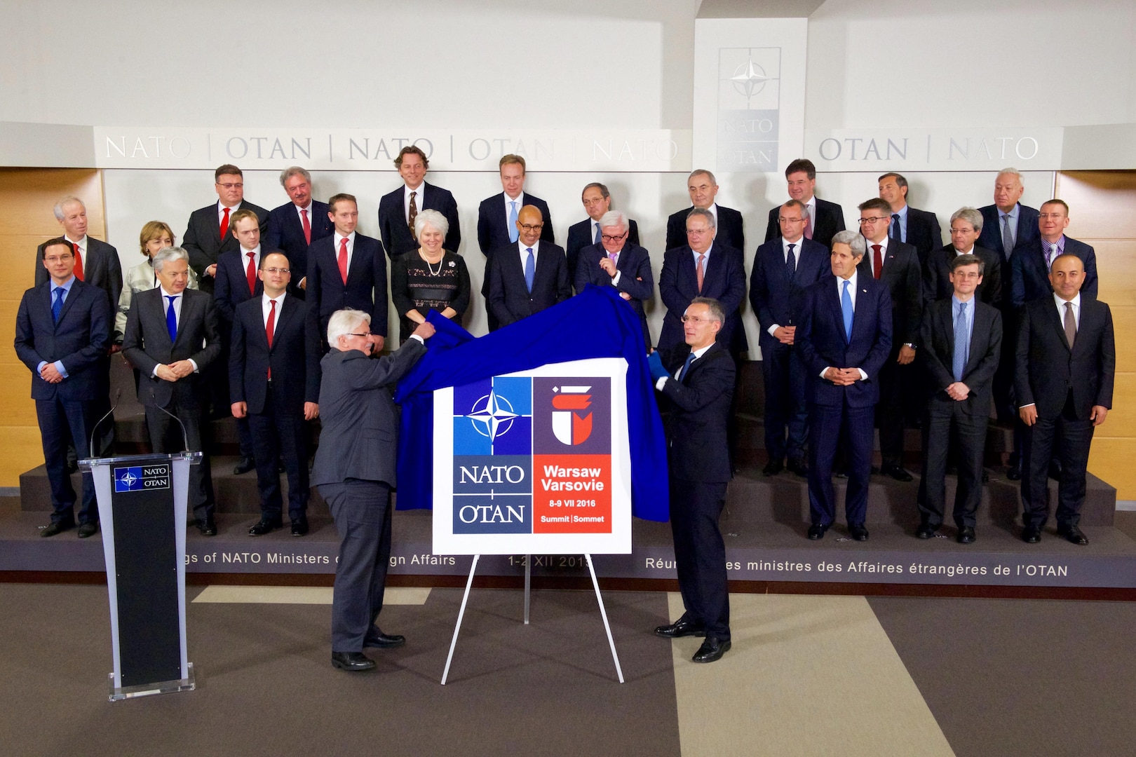 U.S Secretary of State John Kerry and his fellow Foreign Ministers watch as North Atlantic Treaty Organization Secretary General Jens Stoltenberg and Polish Foreign Minister Witold Waszczykowski unveil the logo of next year's NATO Summit Meeting in Warsaw, Poland, during a break at a NATO Ministerial meeting on December 1, 2015, at NATO Headquarters in Brussels, Belgium. [State Department photo/ Public Domain]