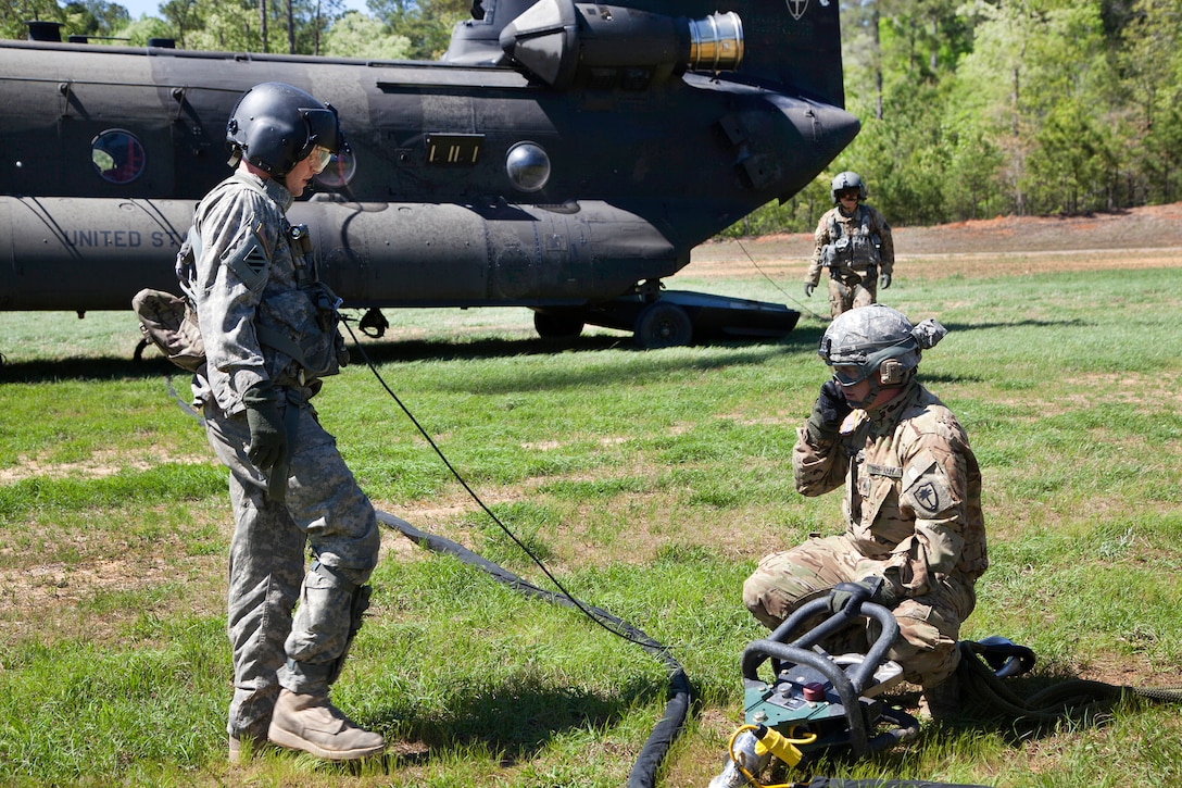 An Army crew chief talks to the pilots in a CH-47D Chinook helicopter as they prepare the cable used to hookup a Humvee during slingload training at Clarks Hill Training Site at Plum Branch, South Carolina, April 2, 2016. South Carolina Army National Guard photo by Capt. Brian Hare