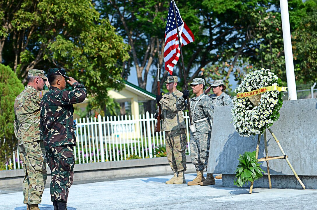Maj. David Tiedeman, 324th PSYOP Company and Maj. Decker Sabangan, 7th Infantry Division, Armed Forces of the Philippines, salute as the National Anthems of the United States and the Philippines are played by the 7th Infantry Division Band during a wreath laying ceremony at the Cabanatuan POW Memorial, April 11, 2016. 