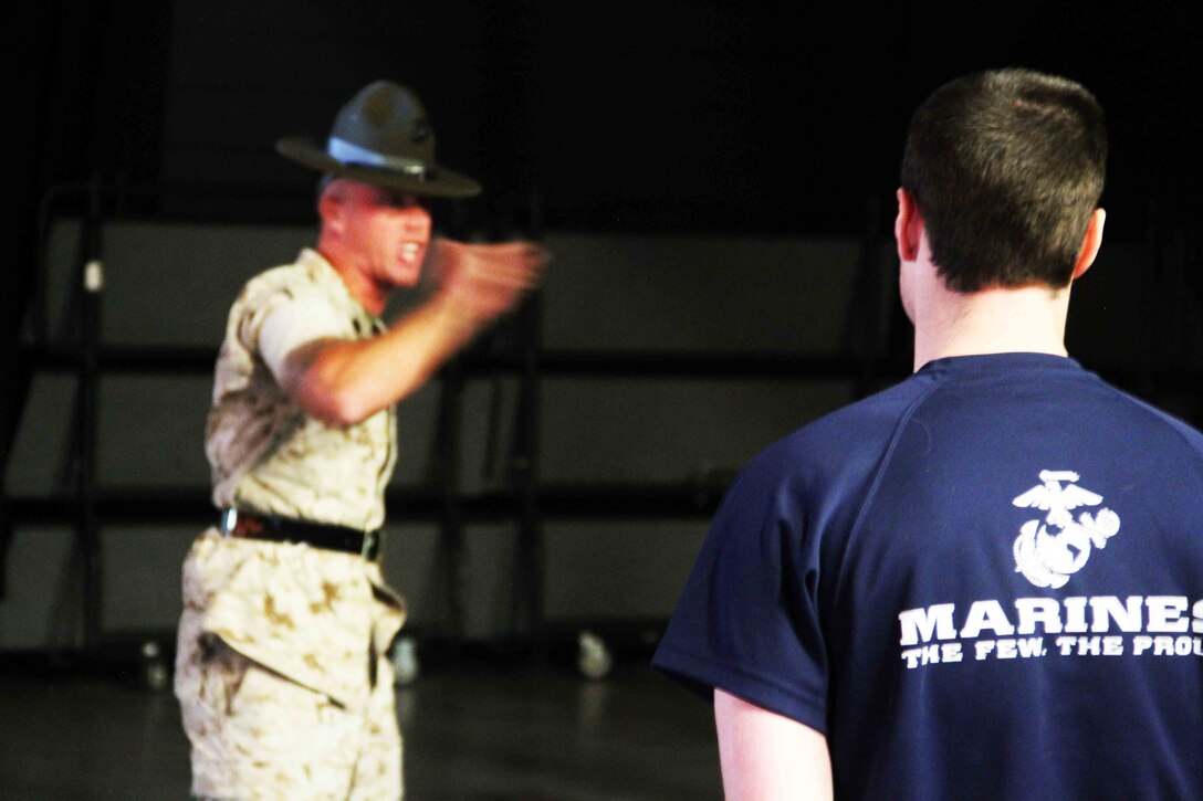 A poolee with Marine Corps Recruiting Station Twin Cities stands at attention as one of the three drill instructors in attendance educate the future Marines on customs and courtesies at the RS Twin Cities Family Night, April 9. During the family night, drill instructors, RS staff and guest speakers informed families on what to expect at recruit training. 