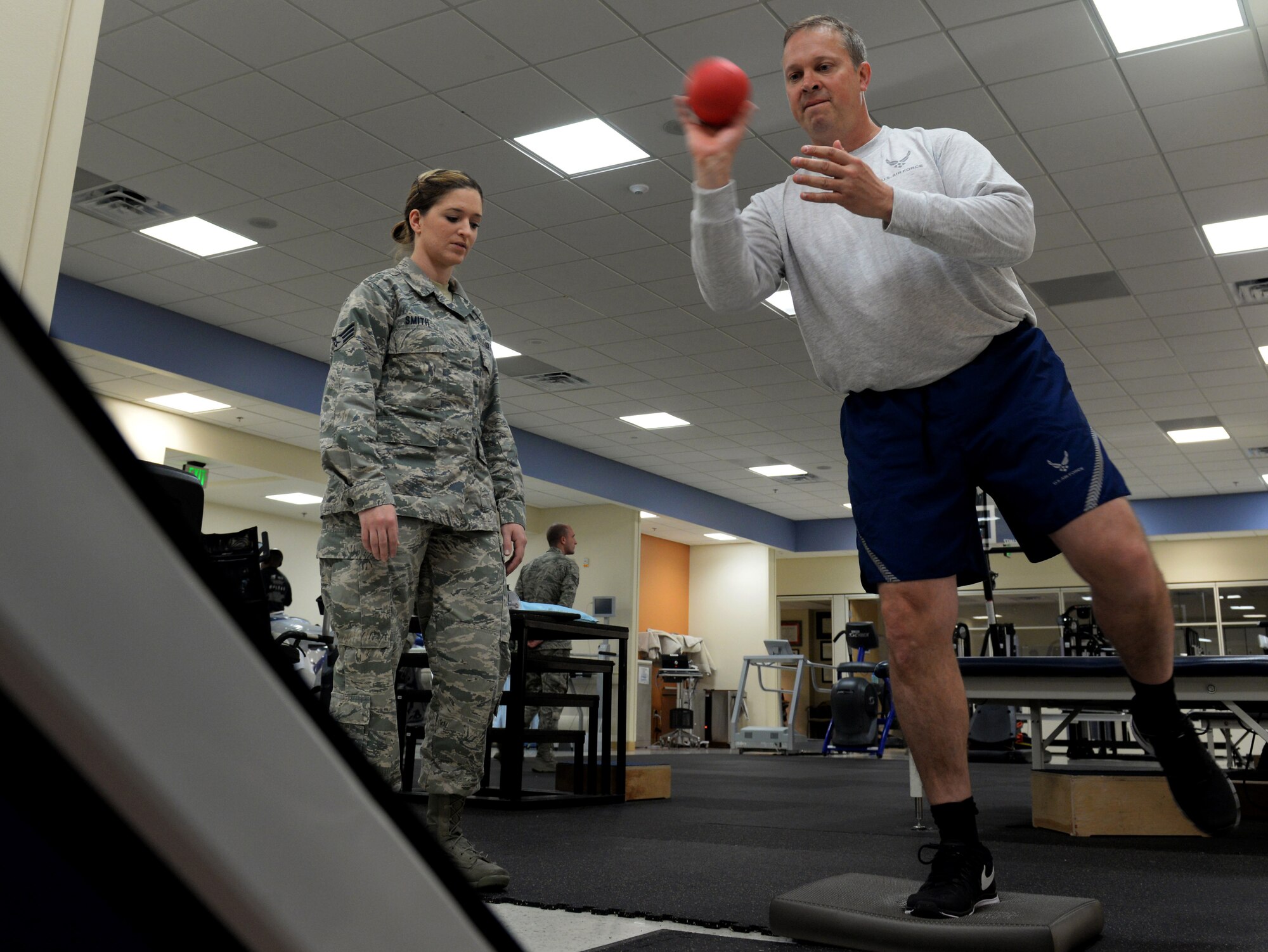 Senior Airman April Smith, 81st Surgical Operations Squadron physical medicine specialist, examines Lt. Col. Thomas Shaak, 81st Medical Support Squadron clinical research lab director, as he balances on one leg in the physical therapy department, April 6, 2016, Keesler Air Force Base, Miss. Shaak is working on his ability to balance and stabilize his knee by standing on a foam pad and throwing a ball into a trampoline. (Air Force Photo by Airman 1st Class Travis Beihl)