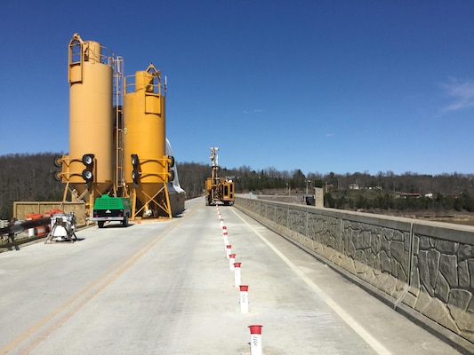 The concrete batch plant is in the foreground atop the Rough River Lake Dam, Ky. The white PVC casings are installed through the embankment to allow drilling and grouting in the rock foundation.