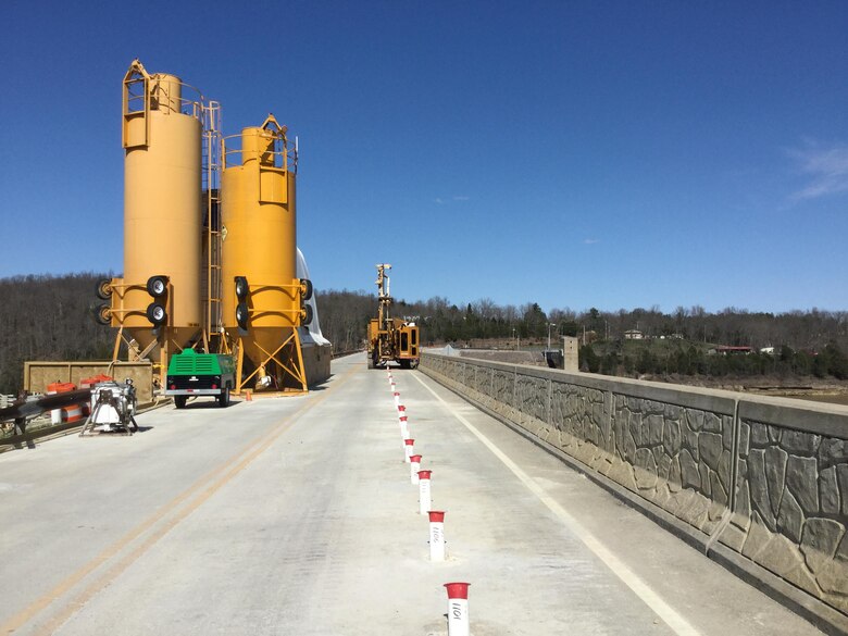 The concrete batch plant is in the foreground atop the Rough River Lake Dam, Ky. The white PVC casings are installed through the embankment to allow drilling and grouting in the rock foundation.