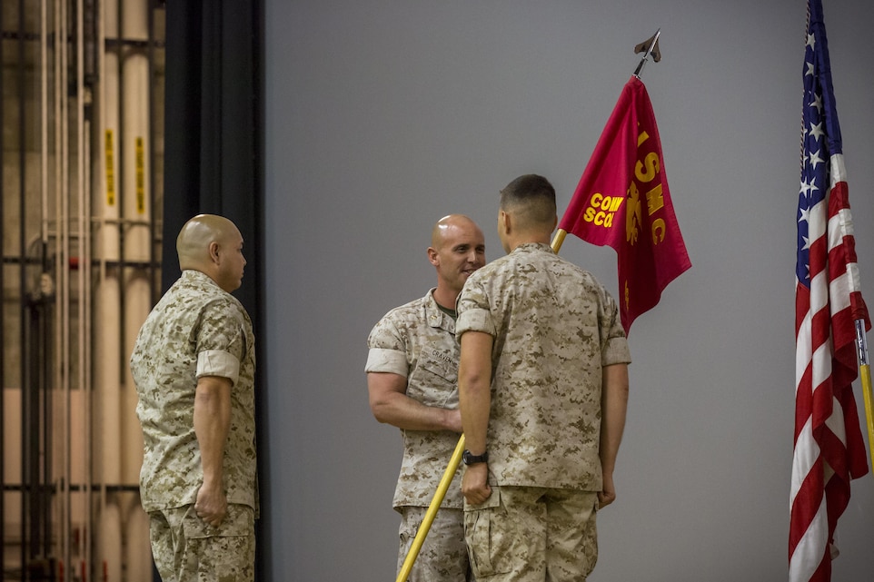 Maj. Chad E. Craven passes the Company D, Communication Training Battalion, Marine Corps Communication-Electronics School, guidon to Capt. Dimitri Stephanoff during a change of command ceremony at the Combat Center theater April 1, 2016. (Official Marine Corps photo by Lance Cpl. Levi Schultz/Released)