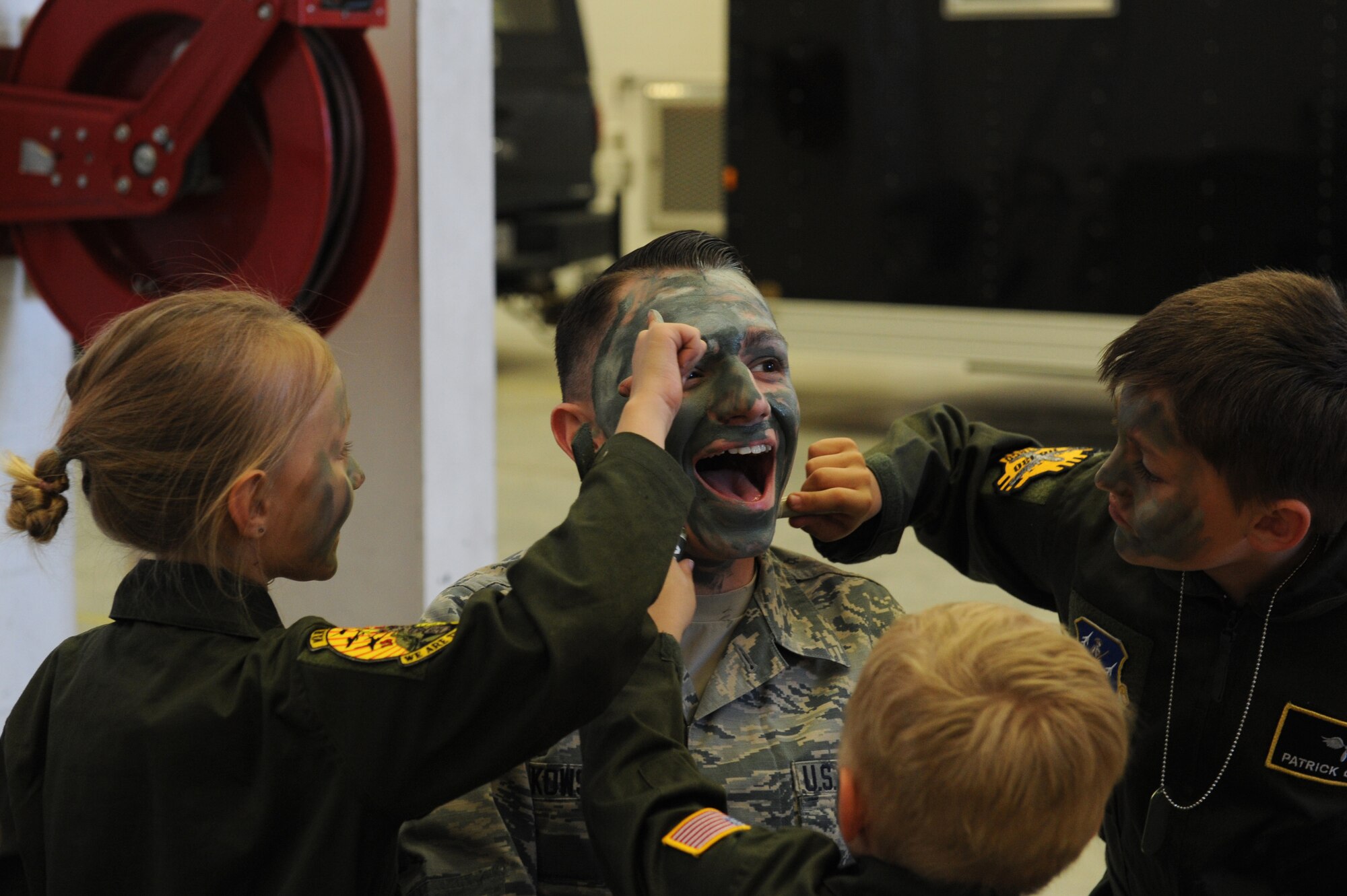 U.S. Air Force Airman 1st Class Randy Oczkowski, 19th Operation Support Squadron Air Traffic Controller, gets his face painted by Lily (left), Henry (bottom middle), and Patrick Griego (right), during a camouflage face painting activity as part of a mock deployment line, April 9, 2016, at Little Rock Air Force Base, Ark. The camouflage face painting station was one of the many activities available during the Kids Understanding Deployment Operations experience, an event geared toward explaining deployment procedures to children. (U.S. Air Force photo by Airman Grace Nichols)