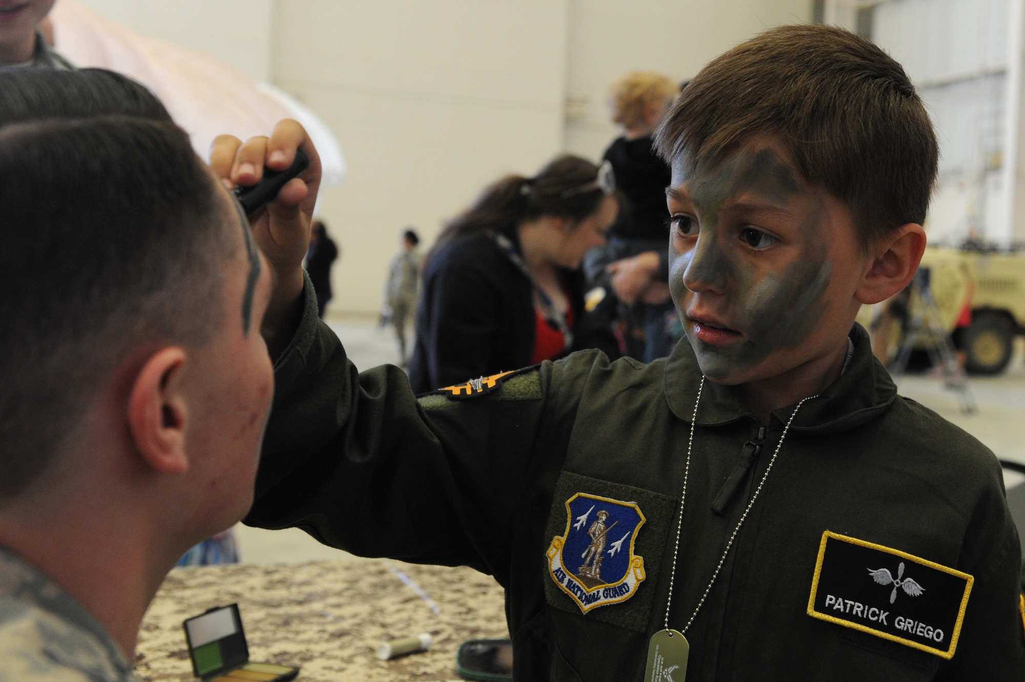 Patrick Griego paints the face of a volunteer during a camouflage face -painting activity as part of a mock deployment line, April 9, 2016, at Little Rock Air Force Base, Ark. The camouflage face painting was one of many activities during the Kids Understanding Deployment Operations experience, an event geared toward explaining deployment procedures to children. (U.S. Air Force photo by Amn Grace Nichols)