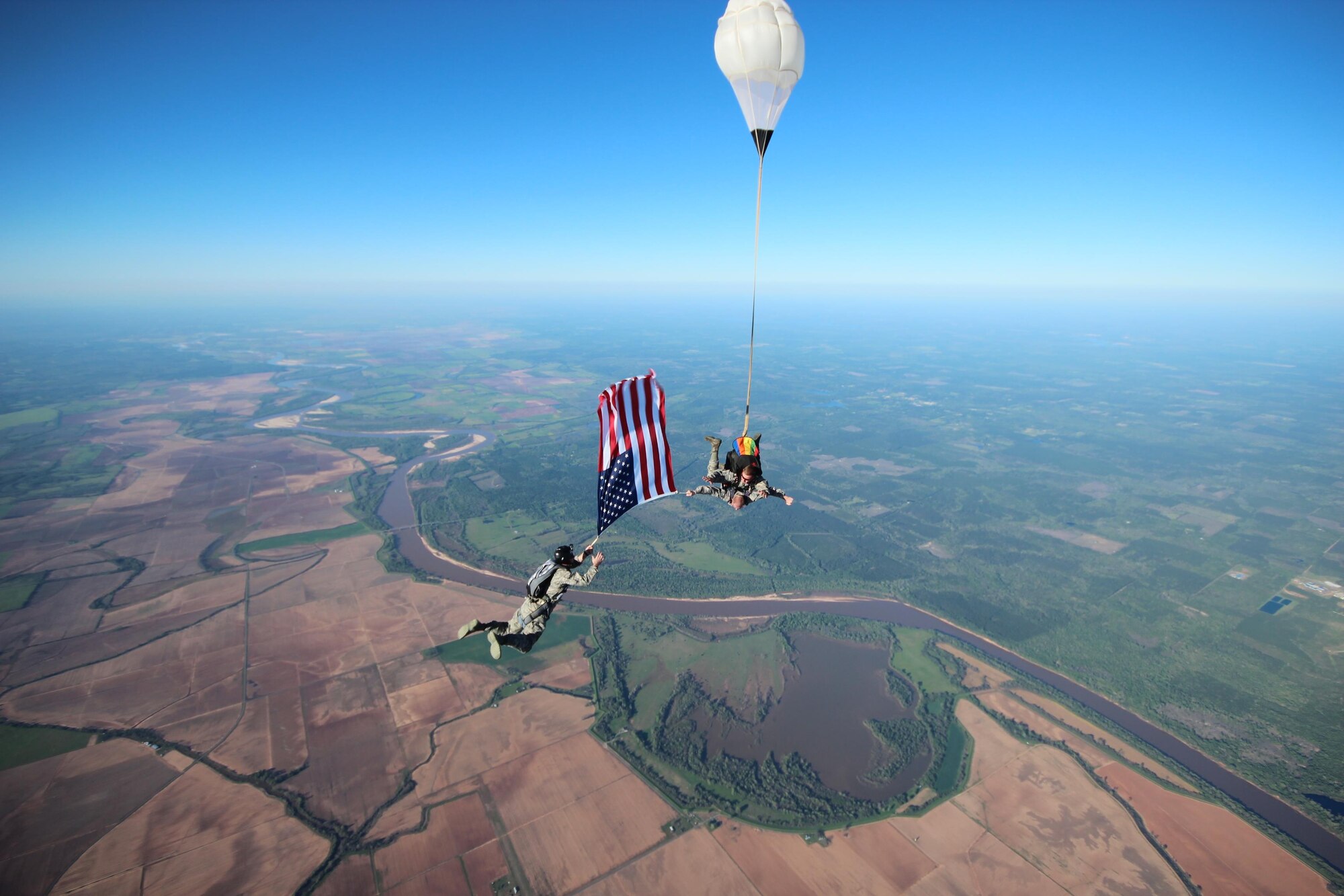 Capt. Jeff Smart, left; Staff Sgt. Matthew Smith, bottom on tandem; and Staff Sgt. Andrew Melanson, top on tandem, free fall with the American flag at 9,000 feet over Gilliam, La., before a re-enlistment ceremony April 5, 2016. Smith and Melanson are both B-52 Stratofortress crew chiefs from the 2nd Maintenance Squadron at Barksdale Air Force Base, La. Smart, who is assigned to the Eighth Air Force at Barksdale AFB, administered the oath of enlistment to Smith in front of the flag the moment they landed from the jump. (Courtesy photo/ Todd Falkenberry) 