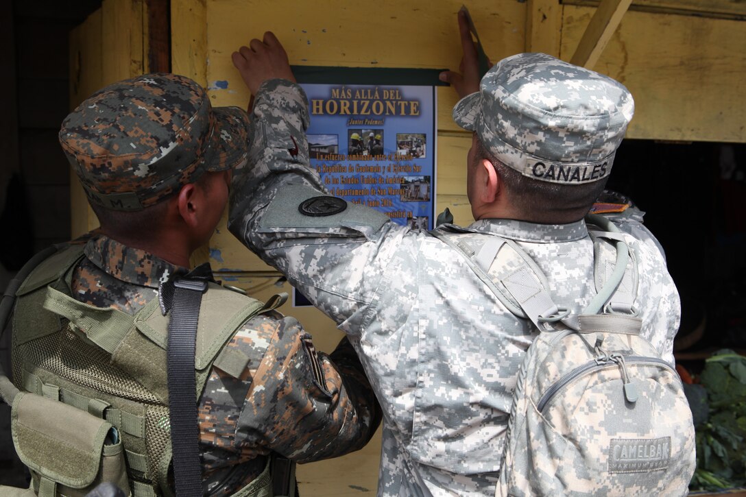 U.S. Army Master Sgt. Andres Canales with the 71st Theatre Information Operation Group with the help of his Guatemalan Army guard tapes a flyer about a medical clinic that will be provided by the U.S. Army at Palo Gordo, Guatemala, March 29, 2016. Task Force Red Wolf and Army South conducts Humanitarian Civil Assistance Training to include tactical level construction projects and Medical Readiness Training Exercises providing medical access and building schools in Guatemala with the Guatemalan Government and non-government agencies from 05MAR16 to 18JUN16 in order to improve the mission readiness of US Forces and to provide a lasting benefit to the people of Guatemala. (U.S. Army photo by Sgt. Prosper Ndow/Released)