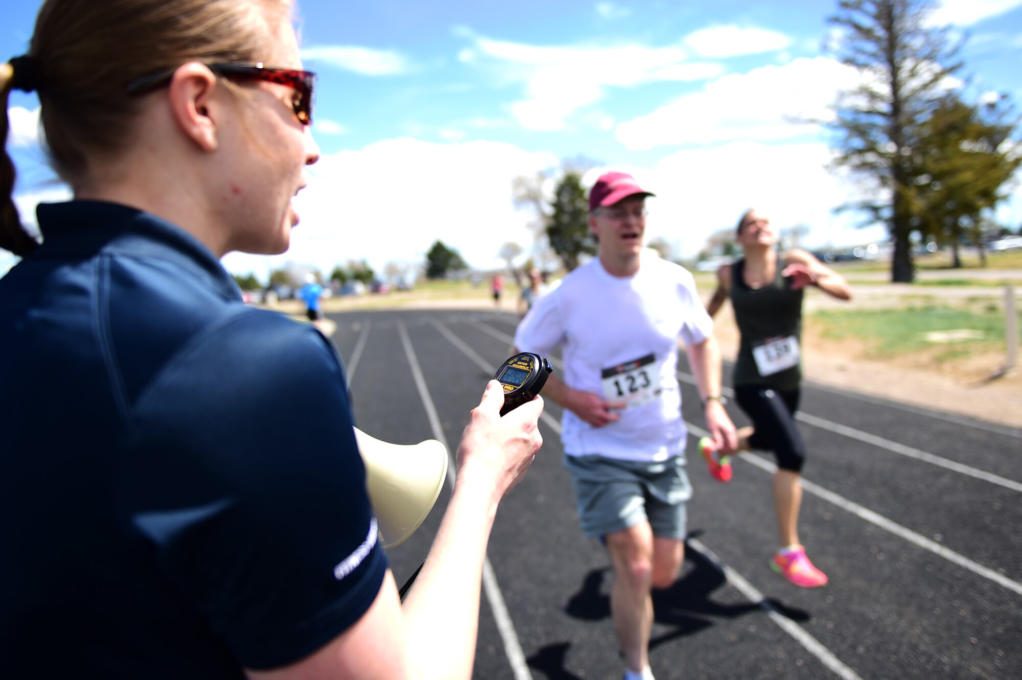 Audra Robinson, 460th Force Support Squadron fitness director, calls the times out for runners as they cross the finish line April 14th, 2016, during the Dash to Distance 5K at the outdoor track on Buckley Air Force Base, Colo. Prizes were awarded for the top male and female finishers, along with Commander’s Cup points, and participants who accumulate 15 or more miles during the series will receive a prize. (U.S. Air Force photo by Senior Airman Racheal E. Watson/Released)