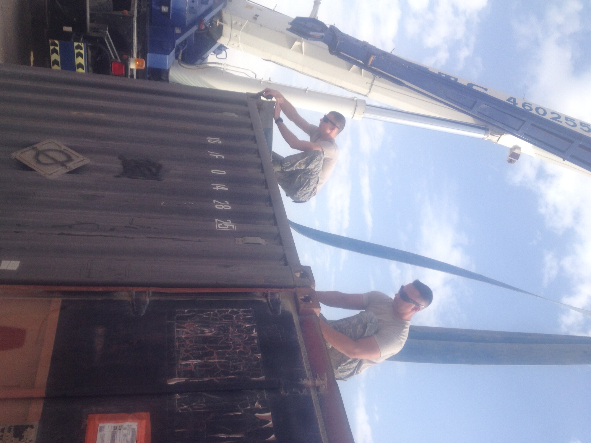 Senior Airmen Thomas Latham (left), unit pass coordinator and Damean Pereira (right), container control officer, both part of the 379th Expeditionary Logistic Readiness Squadron, hook straps onto a container at Al Udeid Air Base, Qatar. The container filled with scrap metal and war reserve materials was one of 80 being prepared for reutilization within the area of responsibility. (U.S. Air Force photo courtesy of Master Sgt. Shobha Parker/Released)