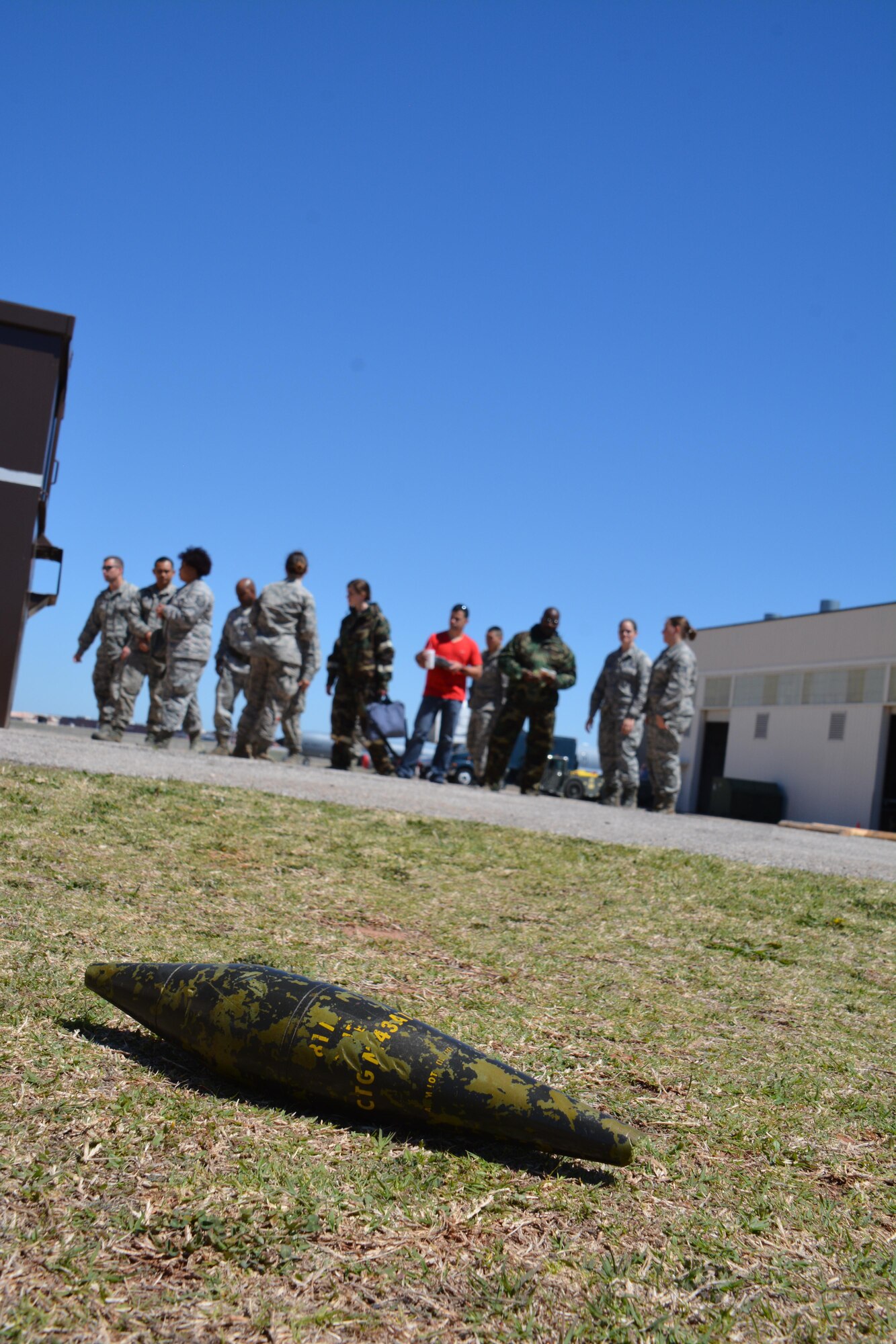 An unidentified explosive ordnance lies on the ground in a training area in the Reserve campus of Tinker Air Force Base, April 3, 2016.  Citizen Airmen in the background are working to identify the UXO as part of an Emergency Management Rodeo during the Super Unit Training Assembly held here April 2-5. The extended training allowed Reservists to complete all annual training and give them a opportunity to take one UTA off.  (U.S. Air Force photo/Maj. Jon Quinlan)