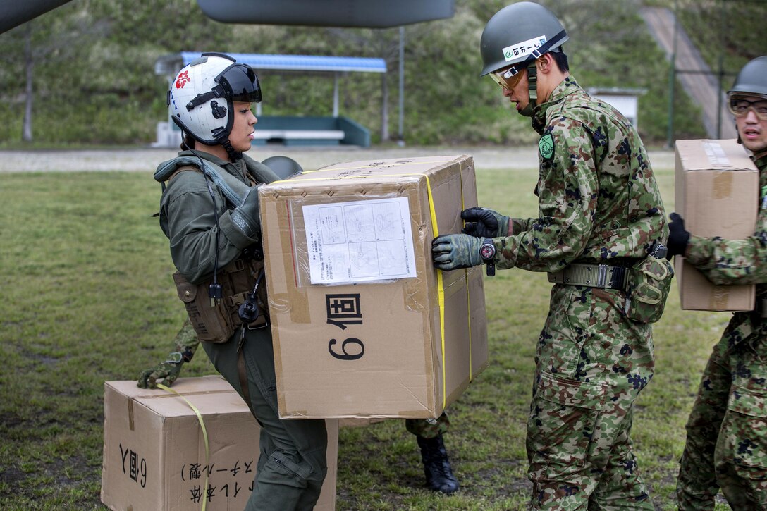 A U.S. Marine Corps crew chief, left, passes a box of humanitarian aid to a Japanese soldier near Kumamoto, Japan, April 18, 2016, to support relief efforts following devastating earthquakes in the region. Marine Corps photo by Cpl. Nathan Wicks