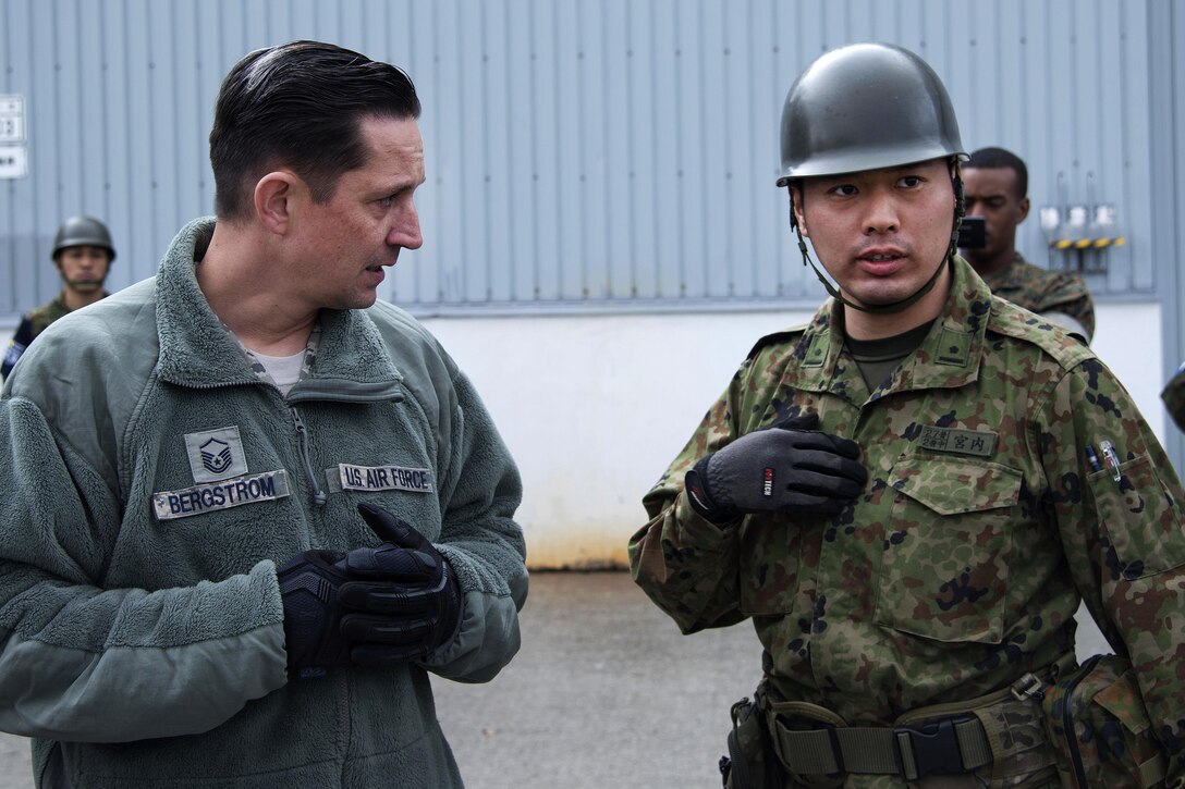 Air Force Master Sgt. Christopher Bergstrom, left, speaks to a Japanese soldier in Chitose, Japan, April 18, 2016. Bergstrom is an air transportation specialist assigned to the 374th Logistics Readiness Squadron. Air Force photo by Staff Sgt. Michael Washburn