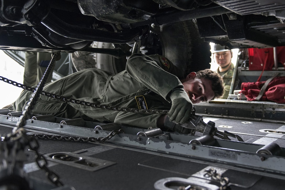 Air Force Senior Airman Dustin Brown uses chains to strap a Japanese army vehicle into a C-130 Hercules aircraft in Chitose, Japan, April 18, 2016. Brown is a loadmaster assigned to the 36th Airlift Squadron. Air Force photo by Staff Sgt. Michael Washburn