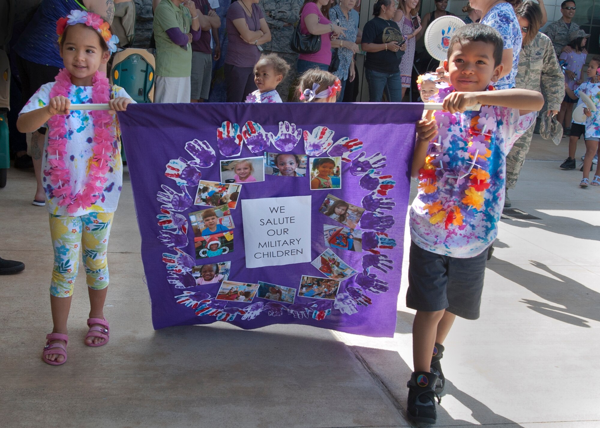 Military children carry a classroom banner in the center-wide student parade held at the Center Drive Child Development Center on Joint Base Pearl Harbor-Hickam, Hawaii, April 15, 2016. Children, parents and leadership took part in activities on the playground at the CDC in celebration of the Month of the Military Child and planted pinwheels in honor of Child Abuse Prevention Month. (U.S. Air Force photo by Capt. Nicole White/Released)