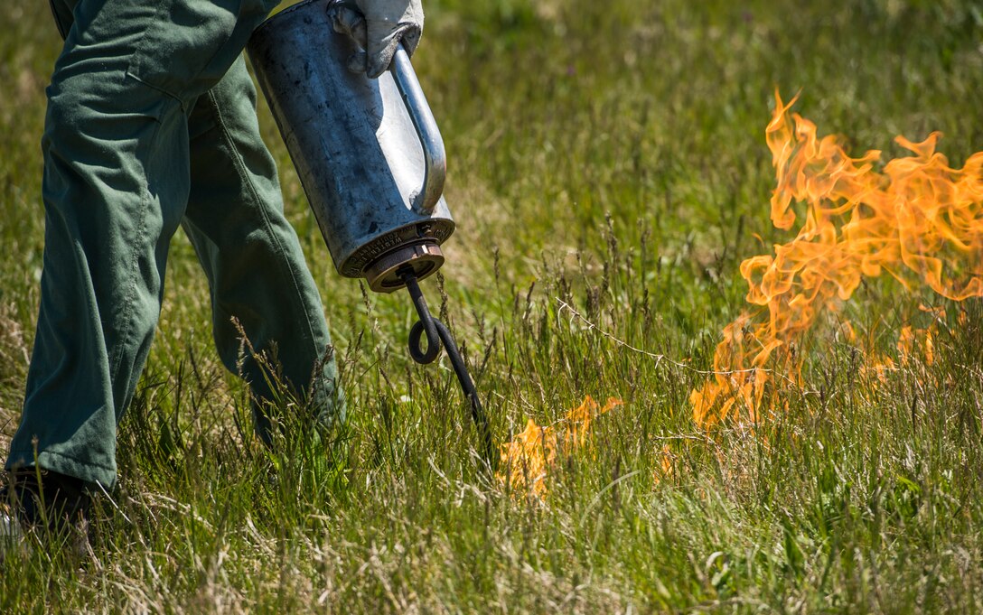A member of the Virginia Department of Forestry uses a drip torch to conduct a controlled burn at Langley Air Force Base, Va., April 17, 2016. Certified technicians burned grass and vegetation that had grown on the flight line infield in preparation for the AirPower over Hampton Roads Open House fireworks display. (U.S. Air Force photo by Senior Airman Kayla Newman)
