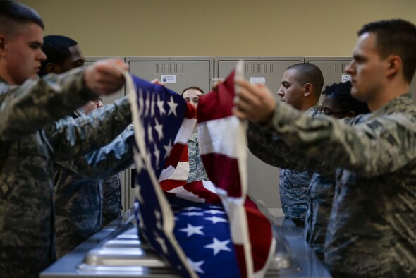 Honor guardsmen in training work with experienced members to practice properly removing a flag from a casket at Mountain Home Air Force Base, Idaho, March 3, 2016. The base honor guard does roughly 300 deatils a year, mostly consisting of funerals. (U.S. Air Force photo by Senior Airman Jessica H. Evans/RELEASED)